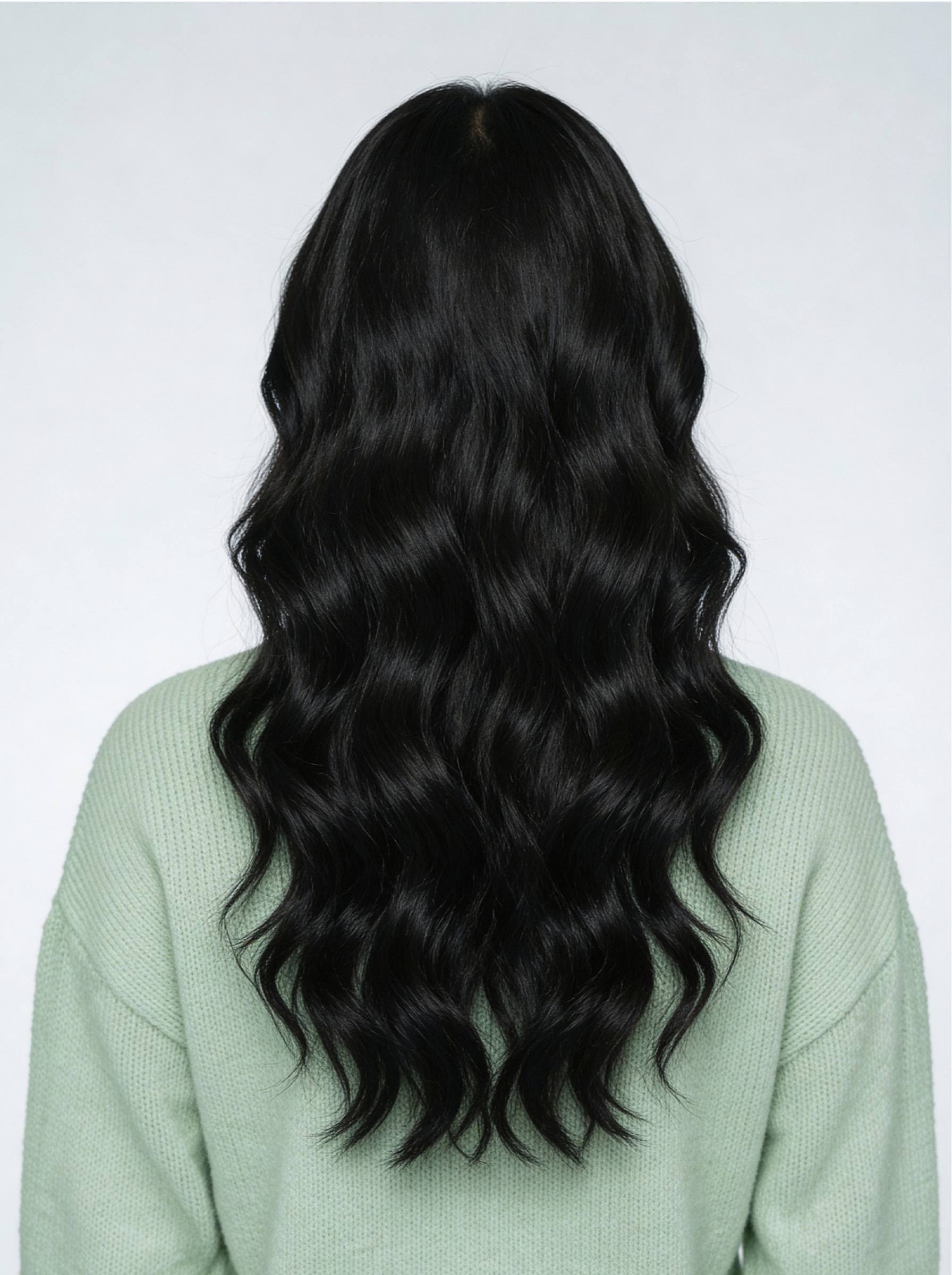 Person with long, wavy black hair wearing a light green sweater on a white background