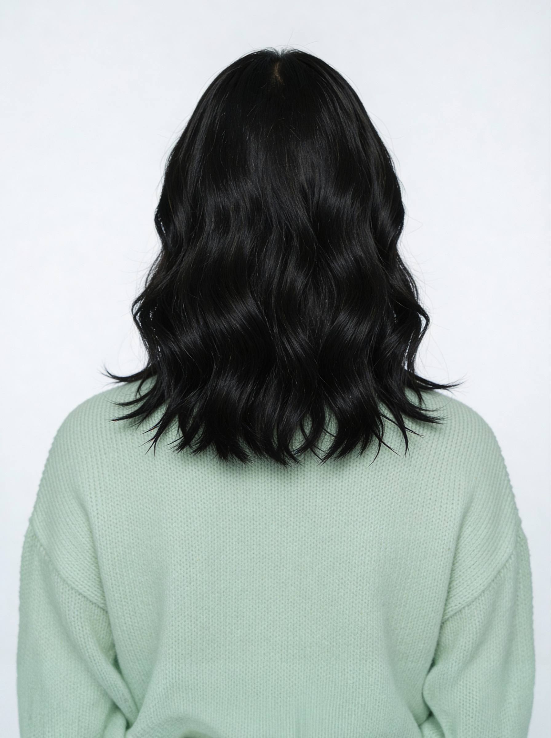Person with long, dark hair wearing a light green sweater on a white background