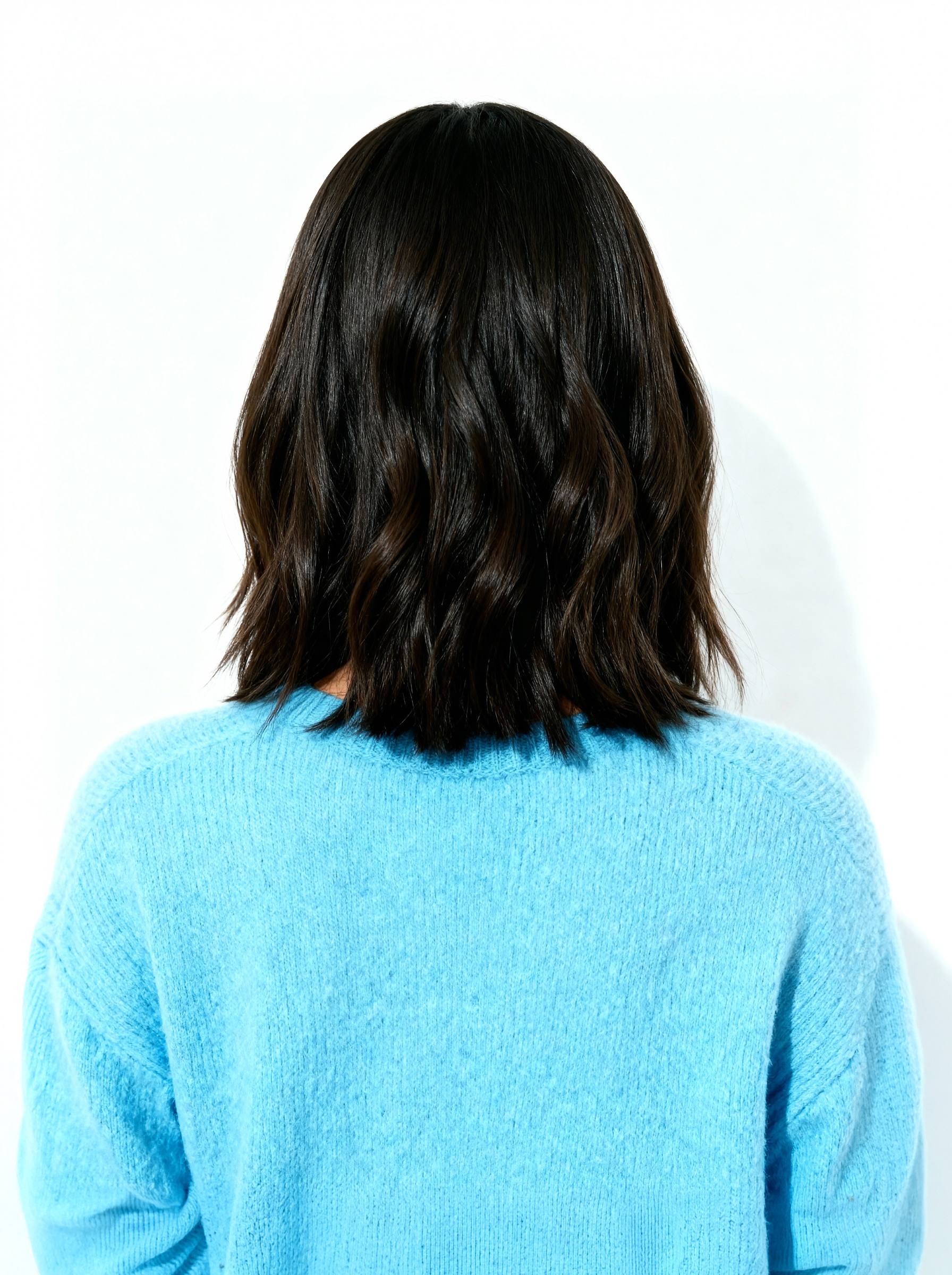 Person wearing a blue sweater with long dark hair on a white background