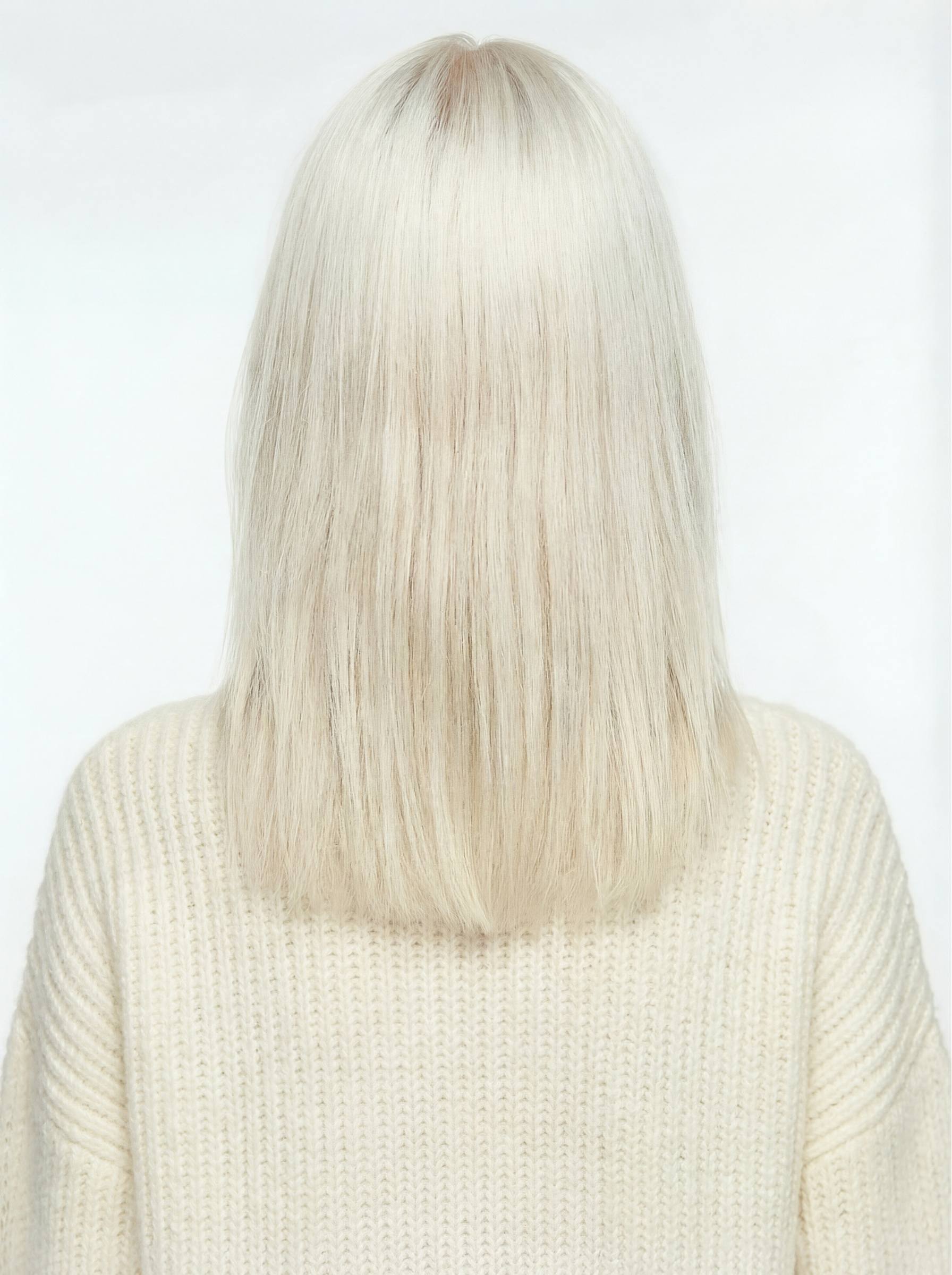 Person with long, straight, platinum blonde hair wearing a light-colored sweater on a white background